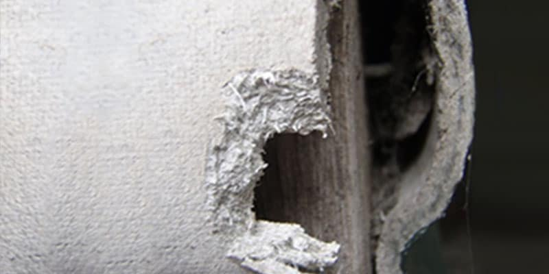 Asbestos pipe insulation exposed inside a wall cavity